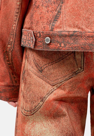 Punainen denim-takki ja housut, joissa on teksturoitu kangas, erottuva ompelu, nappiyksityiskohtia ja huomattava taskusuunnittelu.