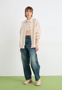 Striped beige oversized shirt, cropped white top, blue wide-leg jeans, and beige sneakers with accents. Green floor background.