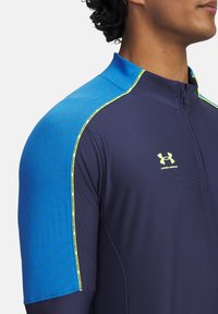 Navy half-zip athletic shirt with a blue shoulder and yellow accent stitching. Made of smooth, textured fabric, featuring a logo on the chest.