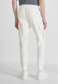 Weiße Baumwoll-Cargohosen mit schmal zulaufenden Beinen, elastischem Bund, zwei Seitentaschen und einer Gesäßtasche. Mit sichtbaren Nähten und gerippten Bündchen.