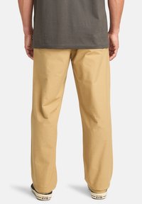 Pantalones de algodón beige con un corte relajado, bolsillos laterales y detalles cosidos, combinados con zapatillas Converse en blanco y negro.