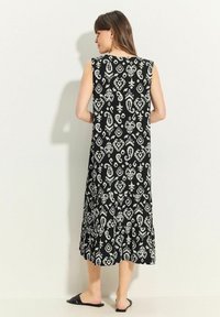 Schwarzes Maxikleid mit weißem Paisleymuster, ärmelloses Design und ausgestelltem Saum. Hergestellt aus leichtem Stoff, mit lockerem Schnitt.