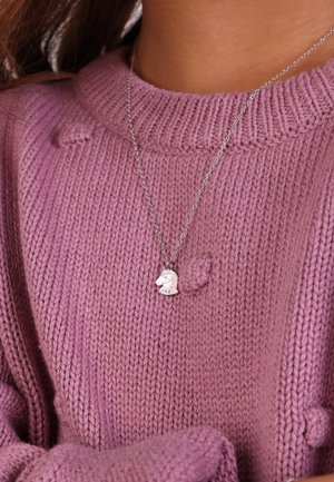 Silberne Halskette mit einem pferdeförmigen Anhänger, der gegen einen weichen, strukturierten, rosa Strickpullover mit geripptem Kragen ruht.