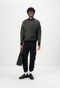 Maglione lavorato a maglia in bianco e nero, vestibilità ampia, orlo a coste, abbinato a pantaloni navy, mocassini neri e una borsa a tracolla nera. Sfondo bianco semplice.