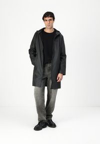 Black waterproof raincoat with a hood, long sleeves, and a front zipper, paired with gray denim jeans and black shoes. Minimalistic design.