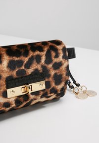 Kopertówka w panterkę wykonana z miękkiej tkaniny, z czarnym, teksturowanym paskiem ze skóry oraz złotymi akcentami metalowymi. Dołączone dwie okrągłe zawieszki.
