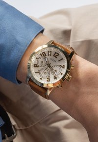 Orologio cronografo in oro e argento con quadrante bianco, cinturino in pelle marrone, numeri grandi e tre sottodial per le funzionalità.