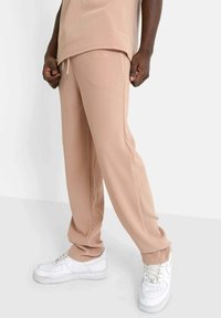 Beige geribde sweatpants met een elastische tailleband en trekkoord, voorzien van zijzakken en een losse pasvorm, gecombineerd met witte sneakers.