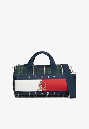 Mała torba typu duffel z granatowym wzorem w kratę, niebieskimi uchwytami, niebieskim regulowanym paskiem na ramię oraz poziomym panelem z logo Tommy Jeans w kolorach czerwony, biały i niebieski.