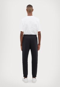 White cotton t-shirt with embossed MK KORS logo on back, paired with black jogger pants featuring elastic waistband and cuffs.