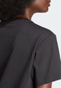 Närbild av en person som bär en enkel mörkgrå t-shirt med kort ärm, som visar nacke, axel och övre del av ryggen.