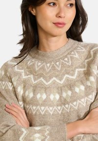 Beige Strickpullover mit weißen und goldenen geometrischen Mustern. Verfügt über einen runden Ausschnitt und eine strukturierte, weiche Oberfläche.