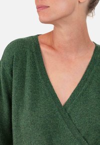 Grüner V-Ausschnitt-Pullover mit weichem, strukturiertem Stoff. Verfügt über ein Wickeldesign und dezente Ziernähte entlang des Halsausschnitts und der Schultern.