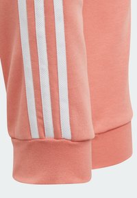 Pantalones de chándal rosa con detalle de tres franjas blancas. Material suave y texturizado, puños ajustados y una silueta ceñida y estilizada.