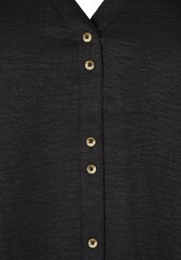 Black shirt featuring a V-neck design, detailed with six beige buttons along the front, made from a textured fabric.