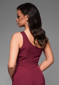 Robe sans manches bordeaux avec un corsage ajusté et une fermeture éclair au dos. Tissu lisse avec un éclat subtil et un design soigné.