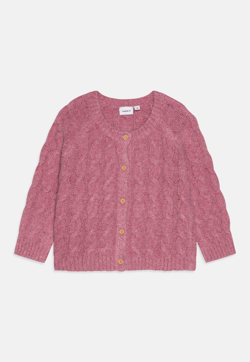 Rozā adīta kardigāna ar kabeli rakstu, apaļu kakla izgriezumu un trim zeltītām pogām priekšpusē. Tam ir garas piedurknes un ribota apakšmalka.