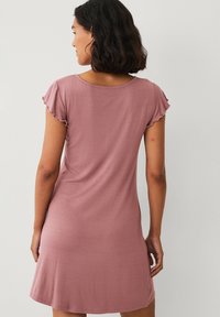 Roze kortgeleemde jurk van zachte stof, met een losse pasvorm en gelegen mouwen voor extra patterndetail en textuur.