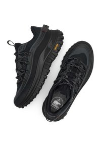 Mustat vaelluskengät, joissa on teksturoitu kangaspäällinen, kumipohja ja näkyvä Vibram-logo. Kenkässä on kontrastiväriset nauhat ja vahvistettu kanta.