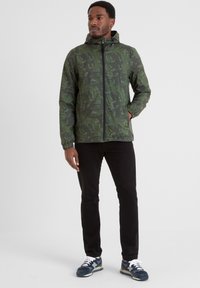 Green patterned zip-up jacket with a hood, featuring elastic cuffs. Worn with black pants and blue athletic shoes with white accents.
