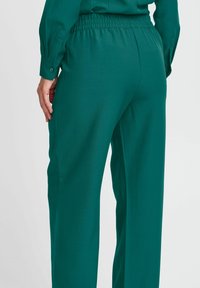 Pantaloni dritti con vita elasticizzata in tessuto teal solido. Presentano tasche laterali e una texture liscia con una silhouette rilassata.