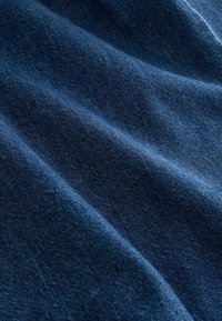 Prim-plan cu material din denim albastru închis, care arată țesătura texturată și pliurile moi.