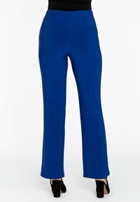 Blauwe rekbare broek met een wijde broekspijpdesign en een elastische tailleband, van achteren weergegeven met zwarte hoge hakken zichtbaar aan de onderkant.