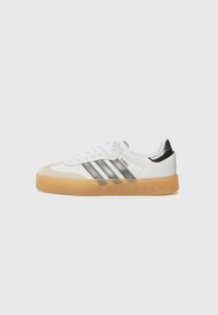 Zapatilla blanca con puntera de ante gris y talón negro. Cuenta con tres rayas grises, cordones blancos y una suela de goma texturizada.