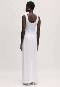 Witte maxi-jurk met een getailleerde bovenstuk, brede banden en een vloeiende, doorschijnende rok. Bevat een subtiele elastische tailleband en een minimalistisch ontwerp.