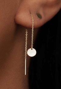 Boucles d'oreilles dorées avec un disque circulaire et une barre mince sur une chaîne délicate. Le design présente une finition polie et un style minimaliste.
