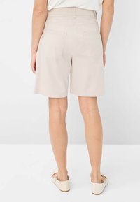 Shorts beige ajustés à taille mi-haute, avec deux poches arrière et une texture lisse, portés avec des chaussures plates de couleur claire.