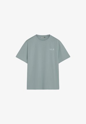 Camiseta azul claro de cuello redondo con mangas cortas y texto "Creative Studio" con un pequeño icono de calavera en la parte superior izquierda del pecho.