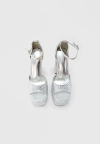 Srebrne sandale z visokimi petami z okraski iz kristalčkov, odprtim prstom, nastavljivim paščkom okoli gležnja in teksturiranim podplatom na platformi.