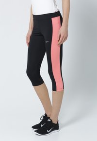 Black capri leggings with a pink side panel, made of stretchy fabric. Features a smooth texture and elastic waistband for comfort. Nike logo is visible.