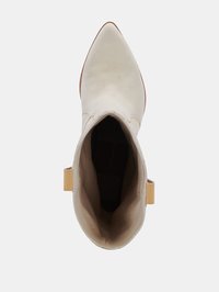 Botín de cuero crema hasta el tobillo con punta afilada, suela plana y una pequeña lengüeta amarilla en el tacón. Textura suave y diseño minimalista.