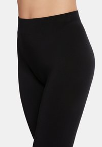 Zwarte leggings met een gladde textuur, hoge tailleband en een aansluitende pasvorm. Ze hebben geen zichtbare naden of patronen.