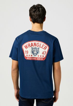 Navyblauwe katoenen T-shirt met een grote geprinte patch op de rug, voorzien van een tijgerafbeelding en de tekst "WRANGLER 1947 WESTERN DENIM".