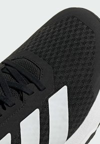 Black athletic shoe featuring a mesh upper, white striped accents, and a textured sole. The design includes black laces and supportive overlays.