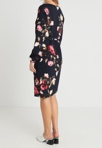 Nawojowa sukienka w kwiaty z długimi rękawami, z różowymi i białymi wzorami kwiatowymi. Gładki materiał, midi długość i dopasowana talia.