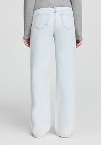 Jeans a gamba larga di un blu chiaro con vita alta, tasche posteriori a toppa e orlo sfrangiato, realizzati in denim con una superficie liscia.