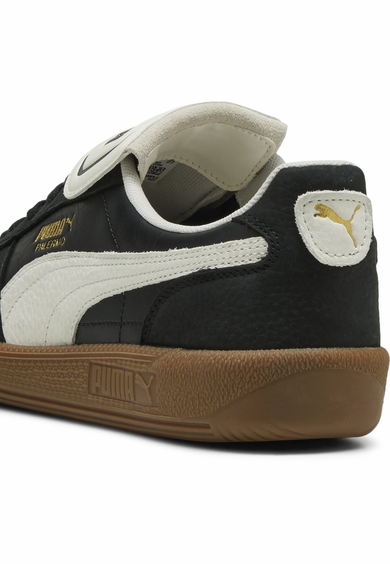 Baskets en cuir noir avec une bande blanche Puma, semelle en caoutchouc, languette et talon rembourrés. Présente des détails de logo doré sur le côté.