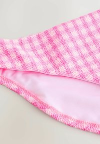 Stickad rosa badkläder med chevronmönster och mjukt foder, med en vågig kantdetalj och kontrasterande inre tyg.