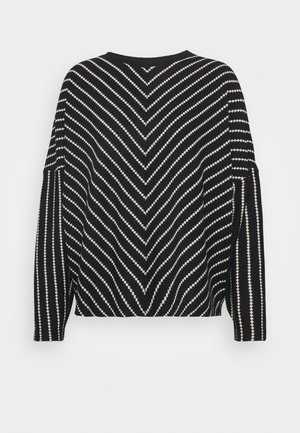 Maglione a righe nero e crema con motivo a zigzag, maniche larghe e vestibilità rilassata. Il materiale sembra morbido con una finitura testurizzata.