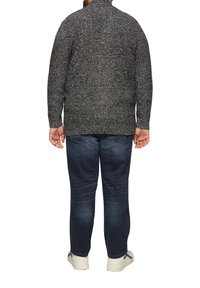 Dunkelgrauer, gestrickter Pullover mit einem strukturierten Muster, ausgeführt mit hohem Kragen und gerippten Bündchen, kombiniert mit dunkelblauem Jeansstoff und hellen Schuhen.
