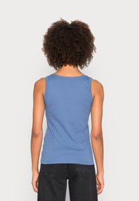 Niebieska bezrękawnikowa koszulka z miękkiej bawełny, z okrągłym dekoltem i dopasowanym krojem. Tył ma czyste wykończenie bez dodatkowych detali.