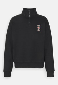 Černá mikina s měkké tkaniny s polo zipem a čtyřmi malými vyšitými logy v červené, zlaté a modré barvě na hrudi.
