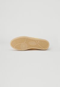 Soletta in gomma di colore giallo chiaro con un motivo a zigzag e un dettaglio di branding circolare, caratterizzata da un design piatto e resistente.
