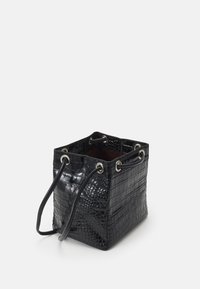 Czarna torba typu bucket z ekologicznej skóry imitującej krokodyla, o kwadratowym kształcie, z dwoma długimi uchwytami i okrągłymi stalowymi elementami. Otwarty górny zamek odsłania brązowe wnętrze.