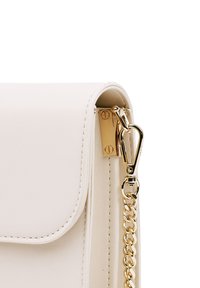 Bílá kožená kabelka s klopou, vybavená zlatými kovovými doplňky a řetízkovým popruhem. Výrazná hladká textura a čisté linie.