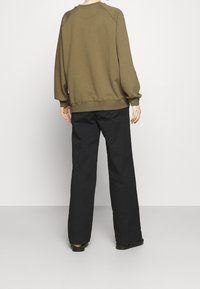 Felpa verde oliva con maniche raglan e polsini a coste, abbinata a pantaloni neri larghi. Design semplice e minimal, senza motivi.